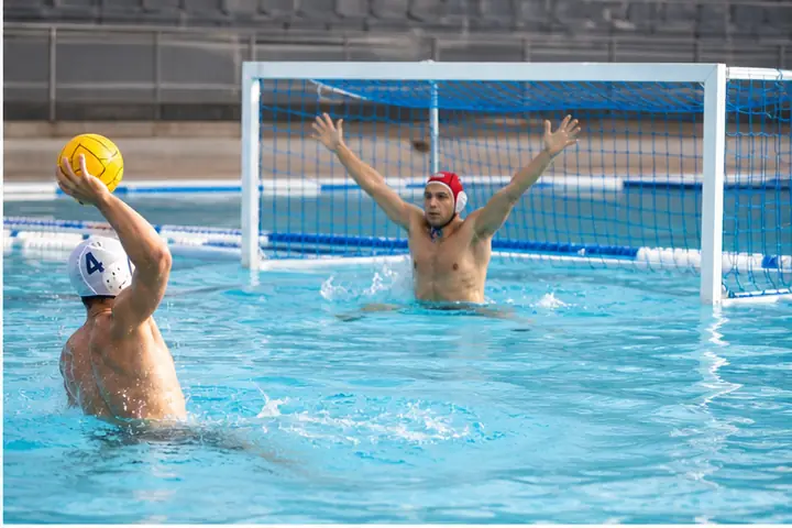 Giocatore tira verso una porta da pallanuoto con rete in piscina.