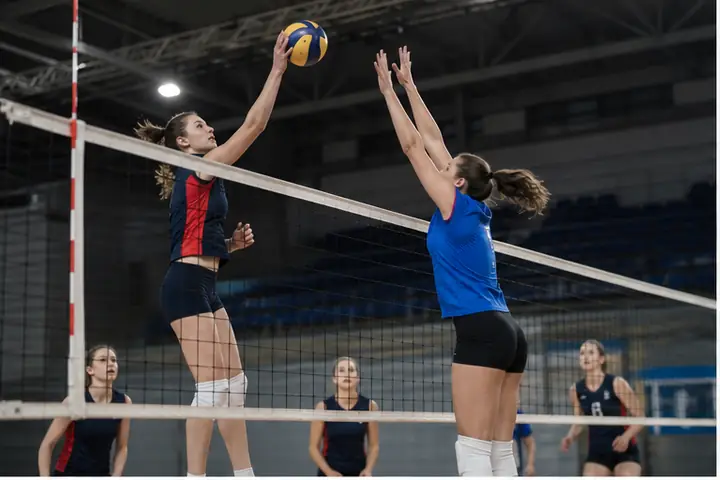 Atlete in azione a rete durante una partita di pallavolo indoor.
