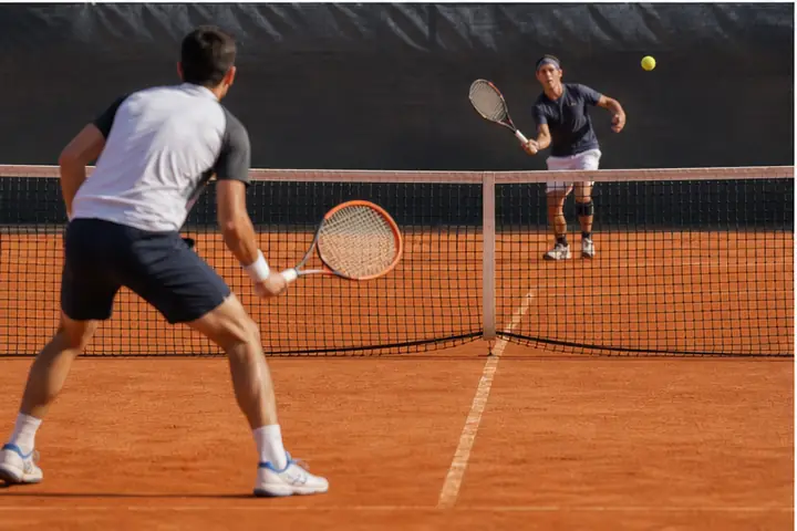 Tennisti in azione con rete regolamentare su campo in terra battuta.